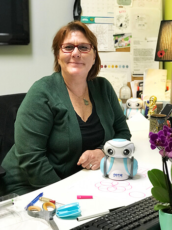 Kelly Recinos, Project Manager at Educational Insights, sits at her desk with creative coding robot, Artie 3000.